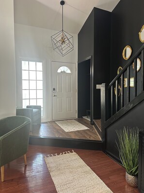 Ein modernes Interieur mit einer Treppe, einem grünen Sessel, einer weißen Tür und einer hängenden Leuchte.