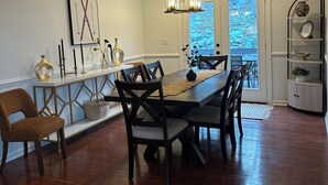 Un coin repas avec une table en bois, des chaises, un lustre et une vue à travers une porte vitrée.