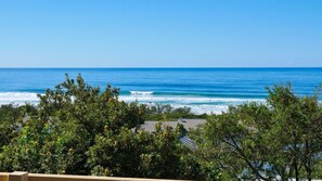 A coastal view with ocean waves, dense green foliage, and a building with a tiled roof. - Carlaminda 4 Peregian Beach (PEREGIAN BEACH)
