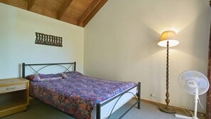 Ein Schlafzimmer mit Bett, Nachttisch, Lampe und Standventilator.