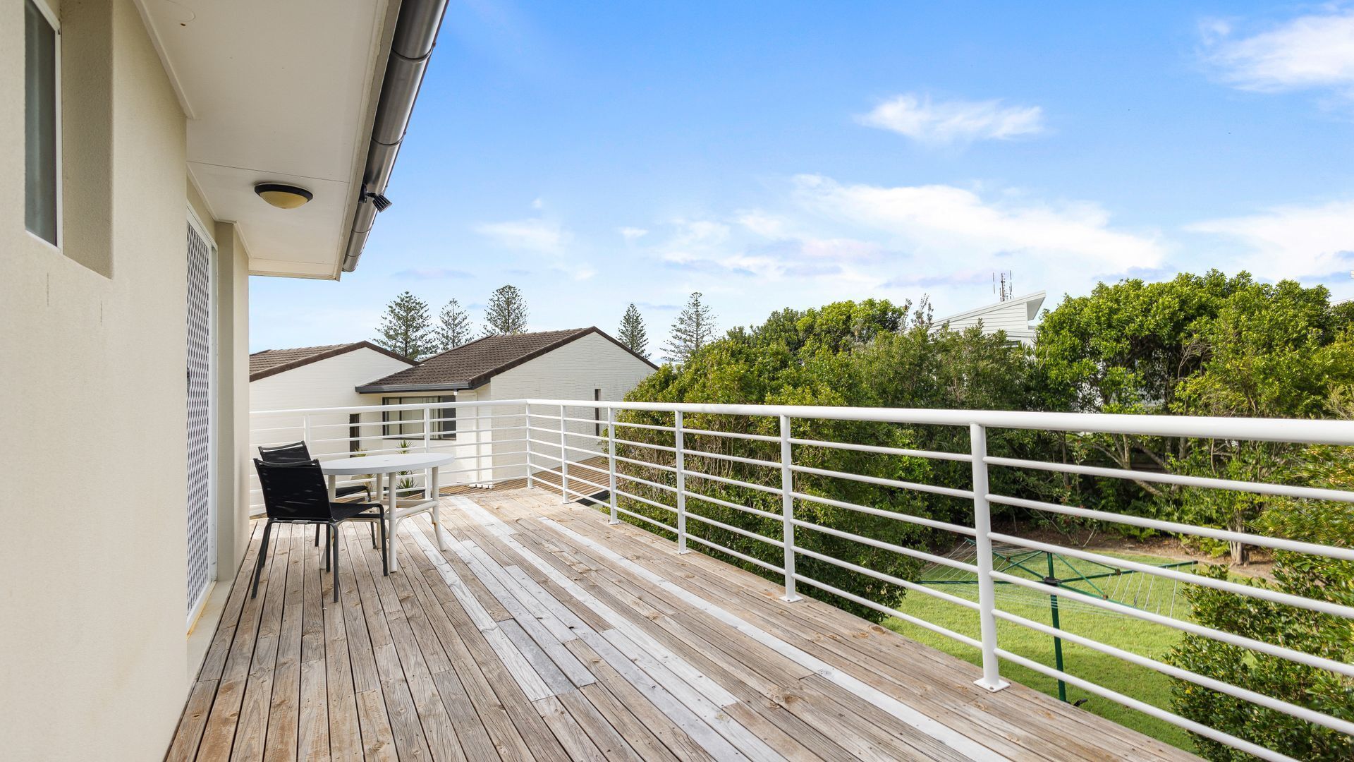 Een houten terras met een witte balustrade, een tafel en twee stoelen.