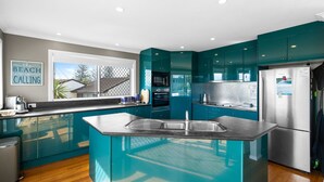 A modern kitchen with teal cabinetry, stainless steel appliances, and a large island with a sink. - Brolga Place Noosa Shire (PEREGIAN BEACH)