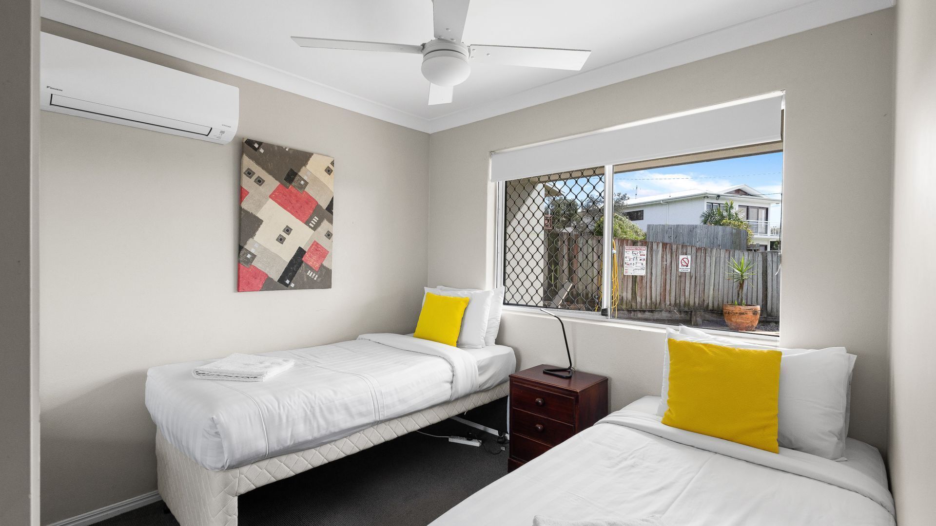 Un dormitorio con dos camas, ventilador de techo, ventana con vistas al exterior y aire acondicionado de pared.