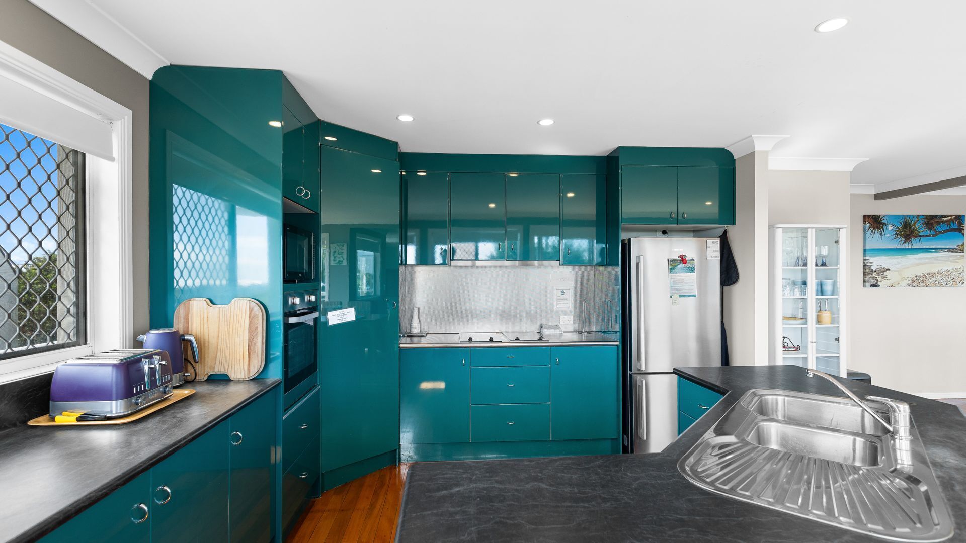 A modern kitchen with teal cabinetry, stainless steel appliances, and a large island with a sink.
