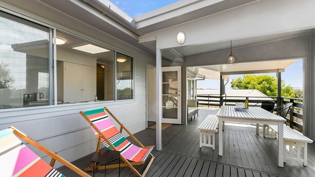 Une terrasse extérieure couverte, aménagée avec des meubles en bois et une chaise à rayures colorées.