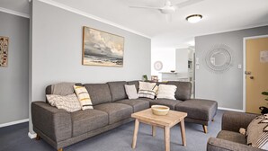 Una sala de estar moderna con un sofá seccional gris, una mesa de centro de madera y un cuadro de una playa.