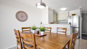 Un comedor con una mesa y sillas de madera, un plato decorativo en la pared y una cocina al fondo.