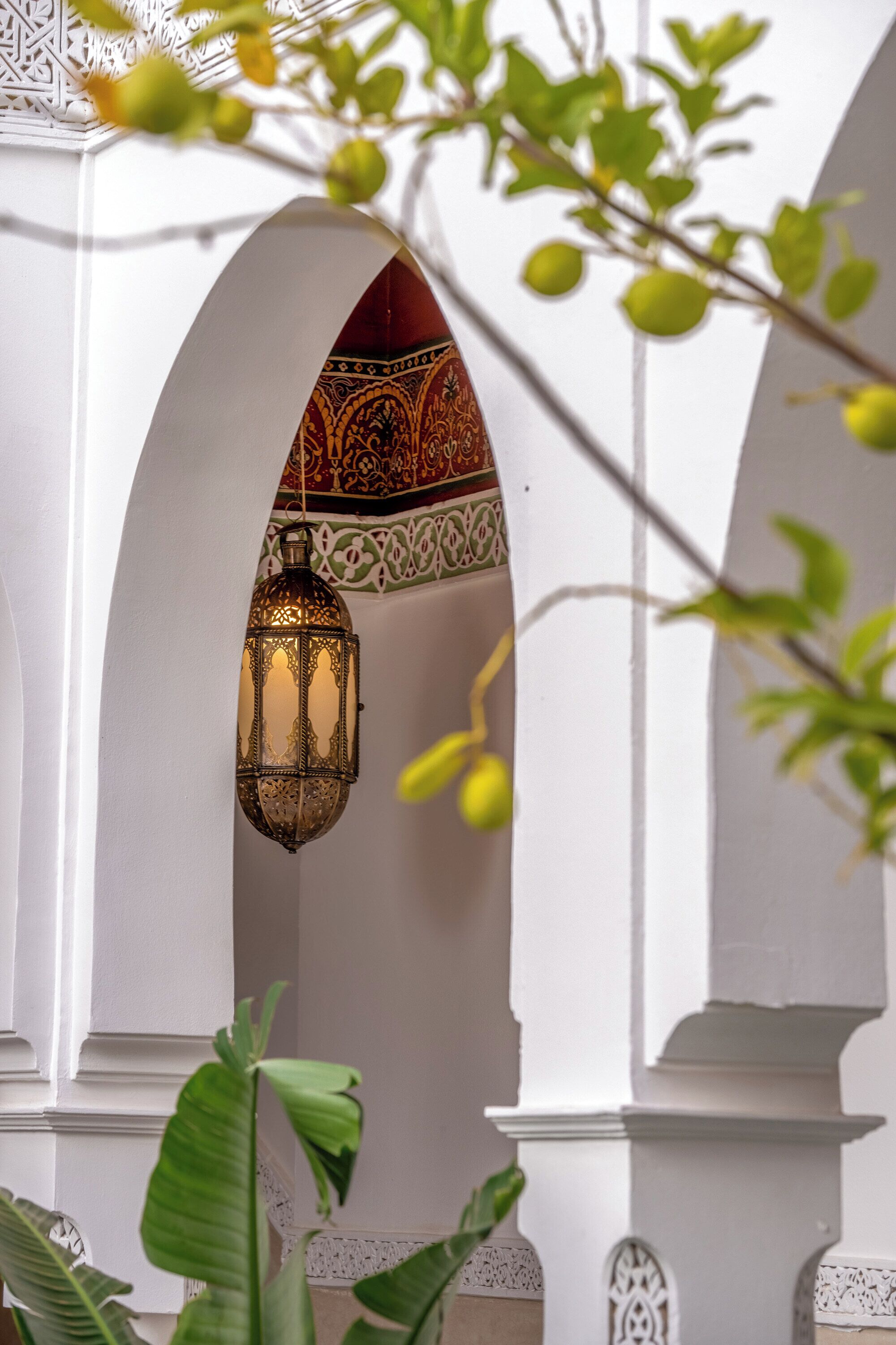 Vue intérieure d’un espace architectural traditionnel, avec une lanterne ornée suspendue au plafond, entourée de murs blancs et d’arcs décoratifs.
