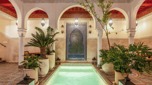 Un espace piscine doté d’un sol carrelé, d’arcades et de plantes en pot.