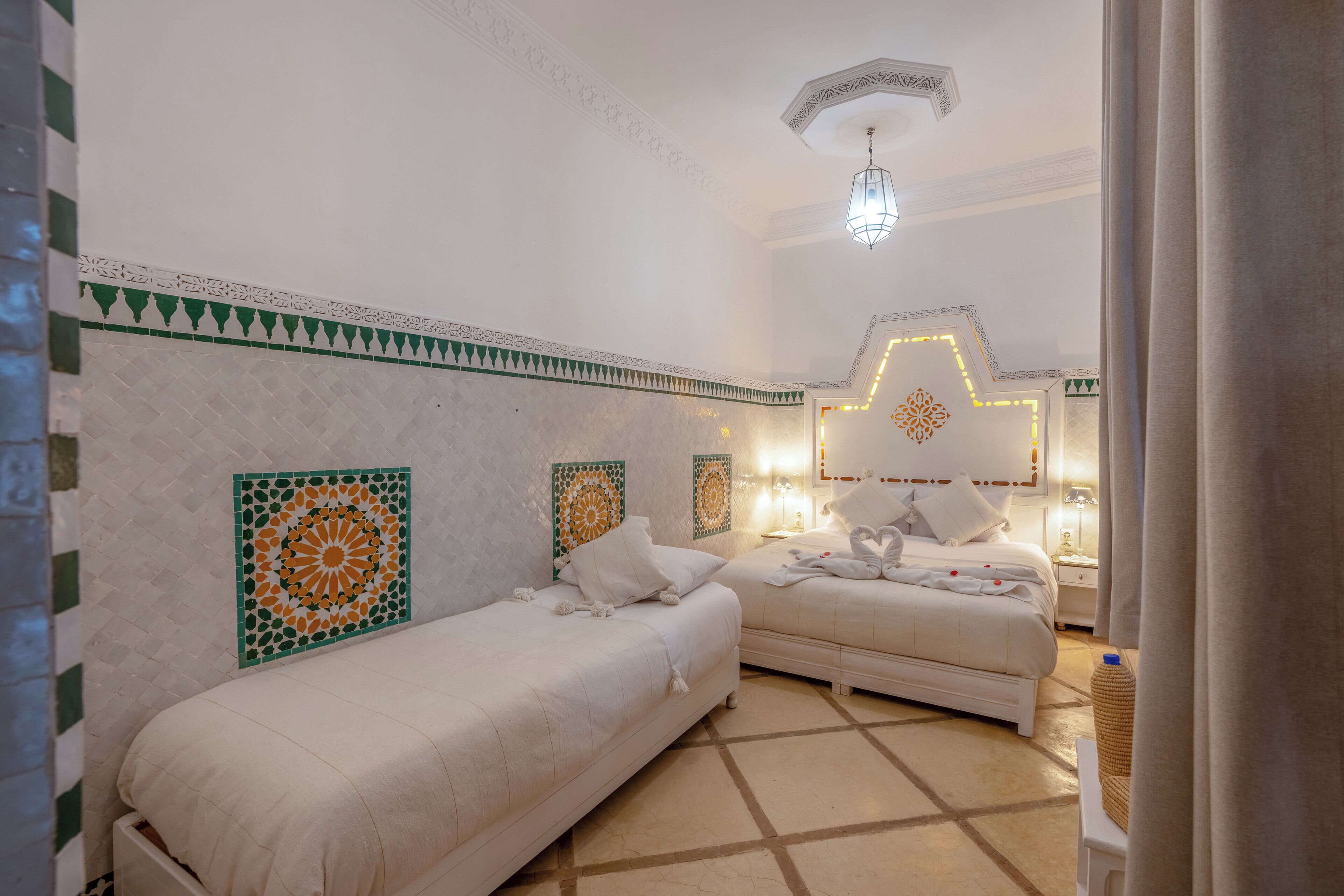 A hotel room with two beds, a patterned wall, a geometric floor design, and a hanging light fixture.