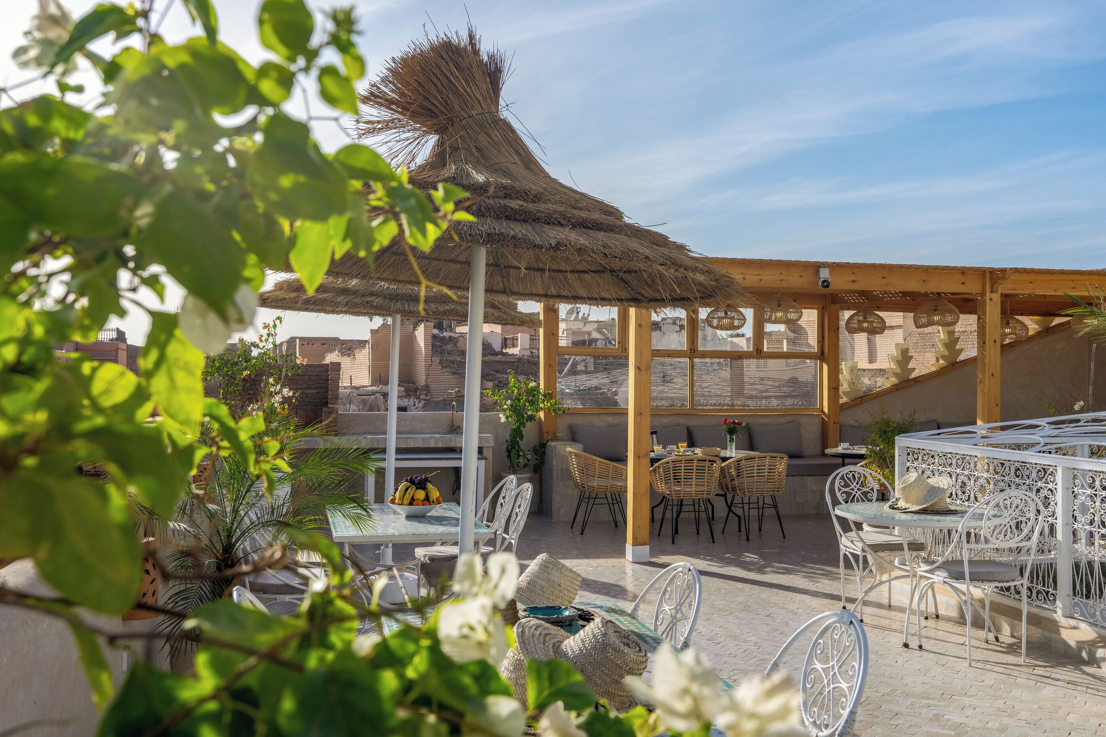 Un espace extérieur aménagé en terrasse, avec des meubles en osier, un toit de chaume et une vue sur le paysage urbain.