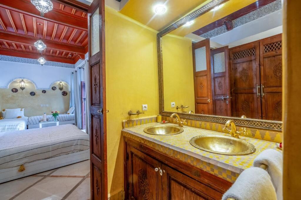 A hotel room with a bed, a double sink, and a large mirror.