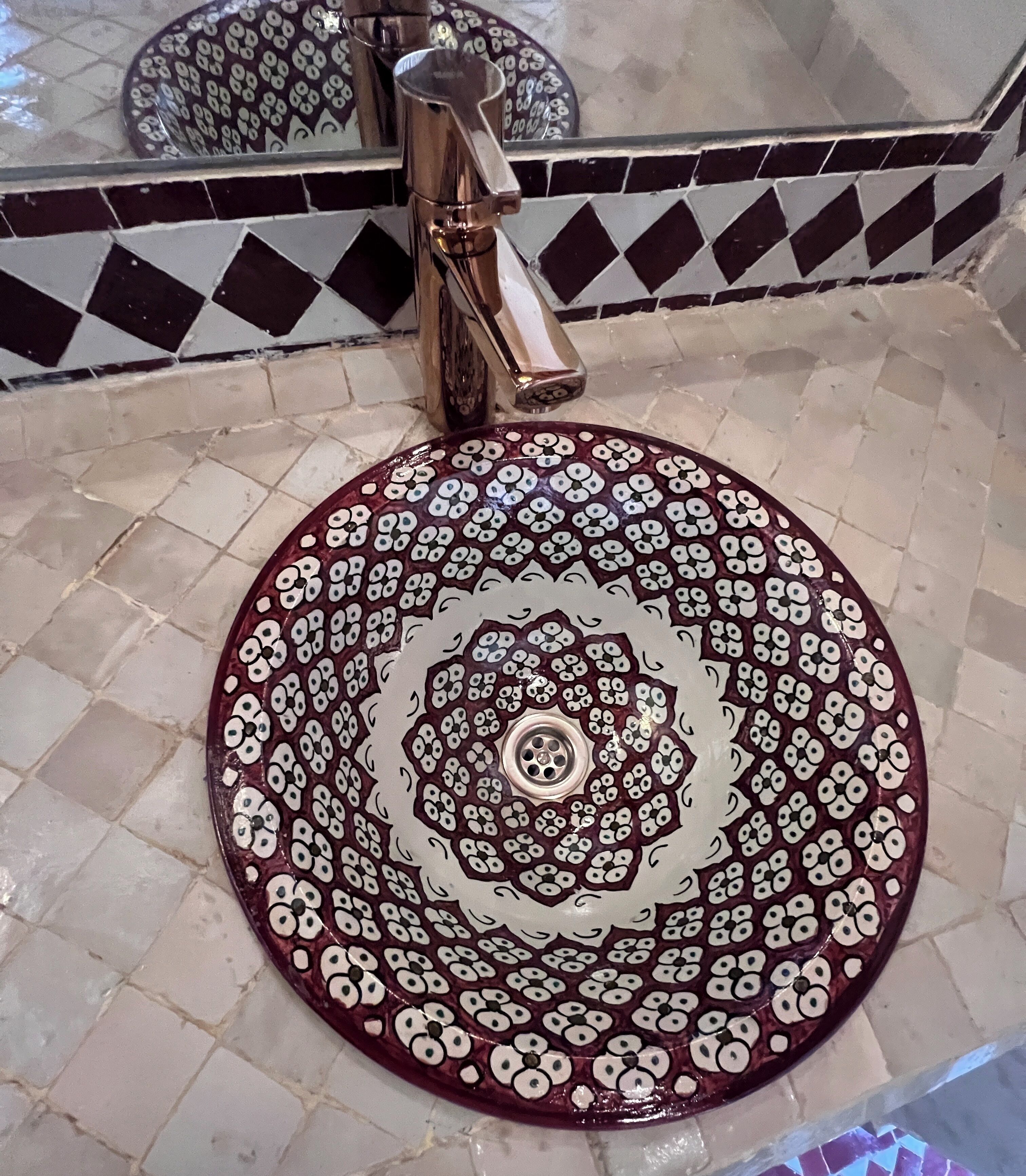 A bathroom with a round sink, a faucet, and a tiled floor with a geometric pattern.