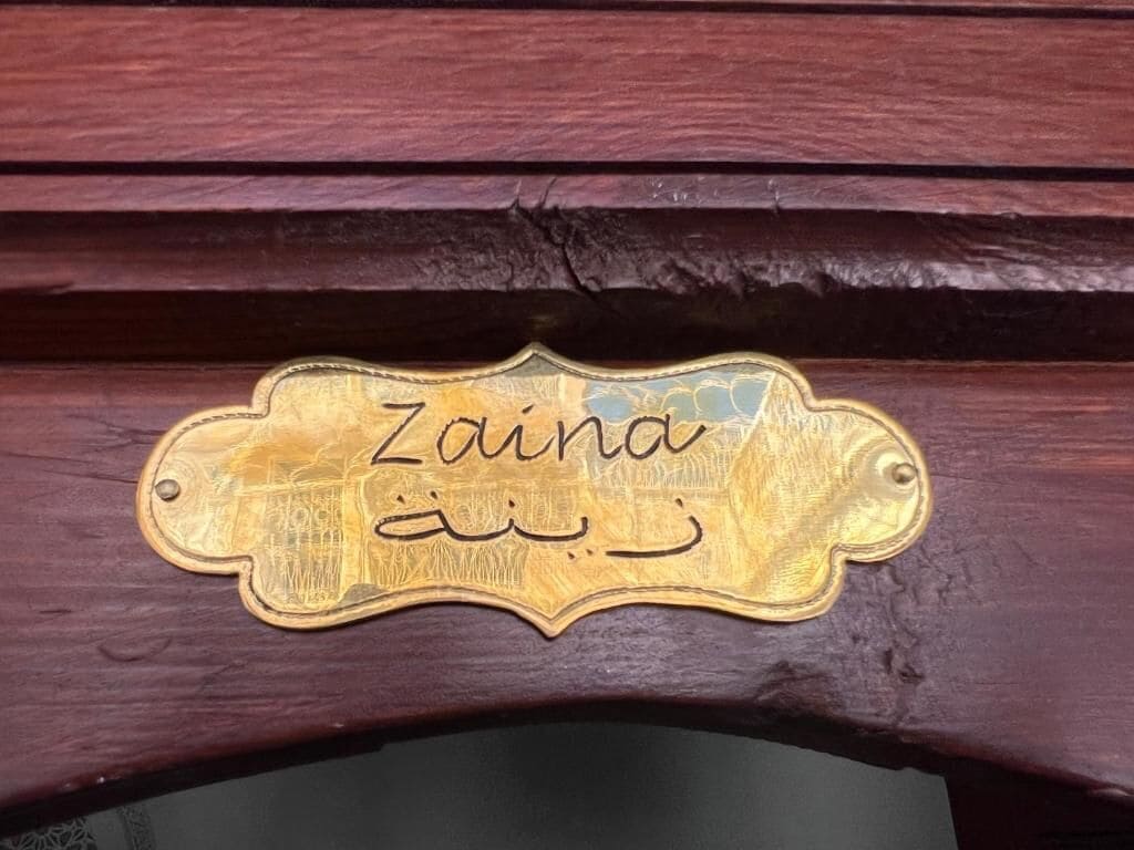 Una placa de latón con el nombre 'Zaima' y escritura árabe.