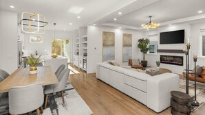A modern living room with a large sofa, a dining area with a wooden table, and a fireplace.