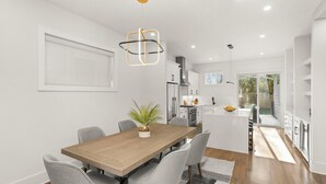 A modern kitchen with white cabinets, a central island, and a dining area with a wooden table and grey chairs.