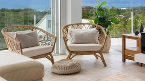 Ein Balkon mit Korbstühlen, einem runden Hocker, einem Holztisch und einem Blumentopf.