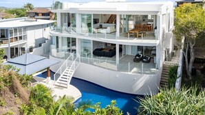 Ein modernes, mehrgeschossiges Haus mit einem verglasten Balkon, einem Pool und einer Treppe, die zum Obergeschoss führt.