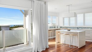 A modern kitchen with a large island, bar stools, and a view of the ocean. - Sea Splash Peregian Beach (PEREGIAN BEACH)