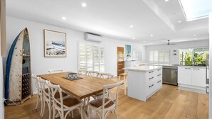 Une cuisine moderne avec des meubles blancs, une table à manger en bois et une planche de surf appuyée contre le mur.