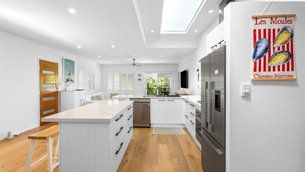 Une cuisine moderne avec des meubles blancs, un grand îlot central, des appareils en acier inoxydable et une lucarne.
