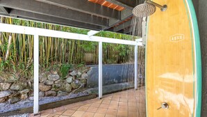 Un espace douche doté d’une porte en bois, d’une structure en métal blanc et de plantes en bambou.