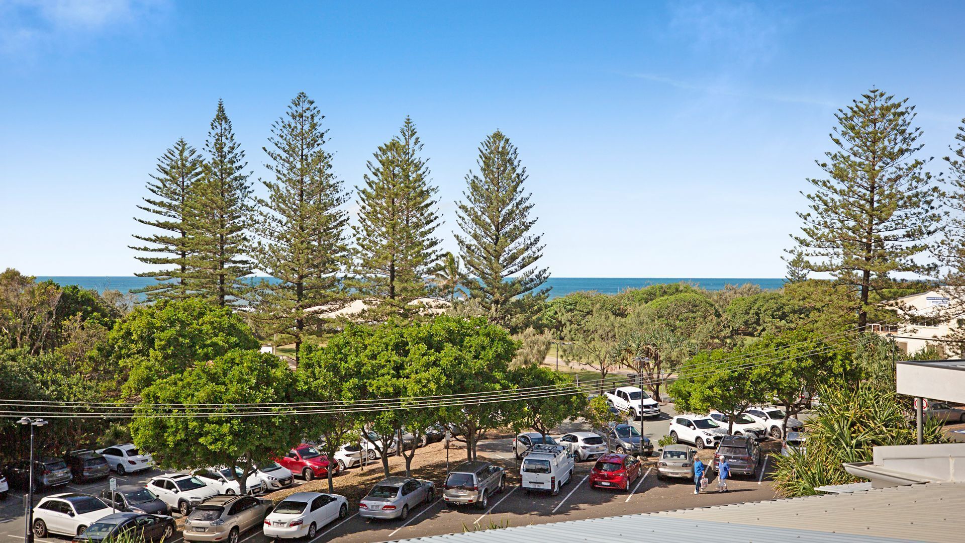 Un parking avec des voitures, des arbres et une vue sur la mer.