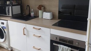 A modern kitchen with white cabinetry, a black stove top, a built-in oven, a microwave, and a washing machine. - Bright apartment in the heart of the Old Port - calm, comfort & ideal location (Marseille)