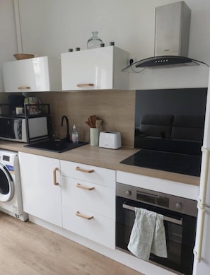 A modern kitchen with white cabinetry, a black stove top, a built-in oven, a microwave, and a washing machine. - Bright apartment in the heart of the Old Port - calm, comfort & ideal location (Marseille)