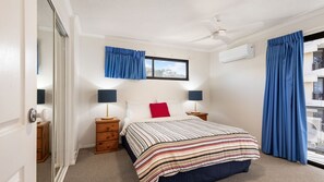 A hotel room with a bed, two bedside tables with lamps, a window with curtains, a ceiling fan, and an air conditioning unit. - Phoenix 8 Coolum Beach (Coolum Beach)