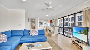 Ein modernes Wohnzimmer mit einem blauen Sofa, einem Couchtisch, einem Fernseher und einem Deckenventilator.