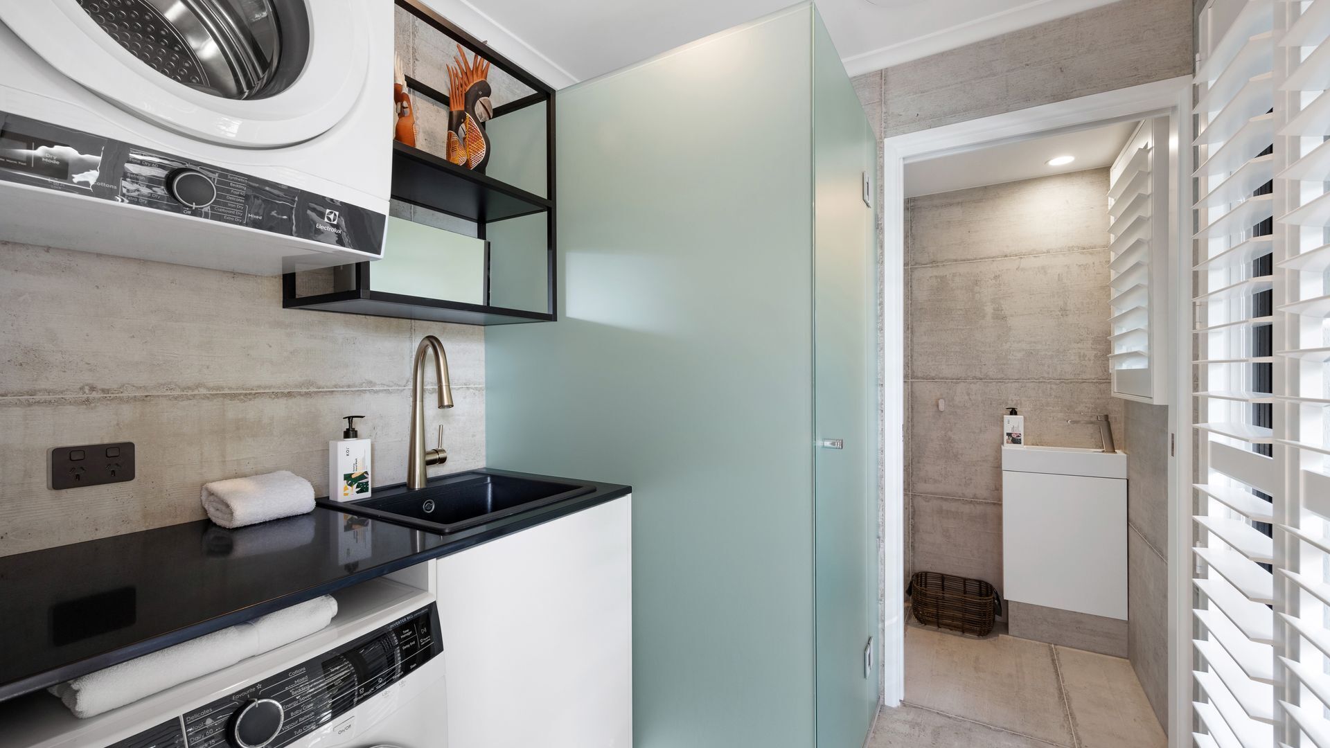 A modern bathroom with a black sink, a built-in washing machine, and a shower area with a white shower enclosure.