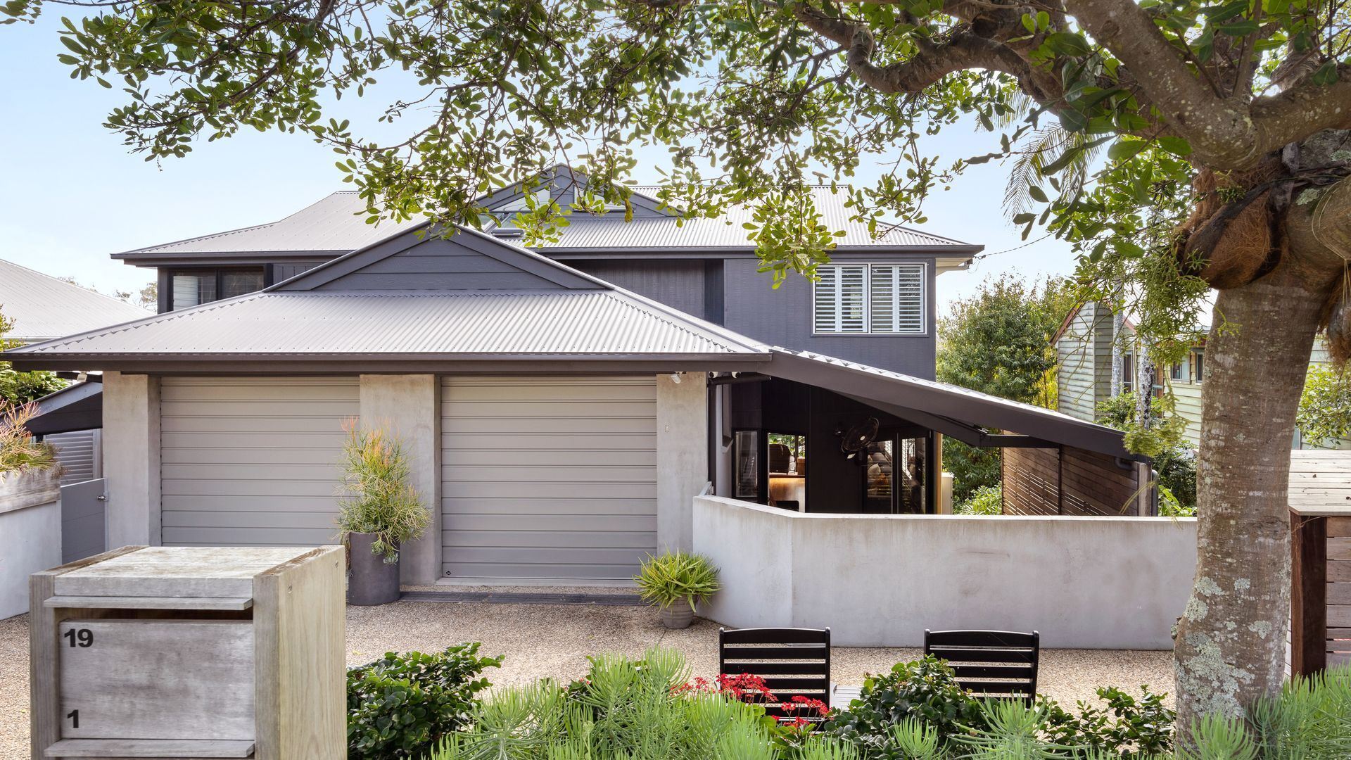 A modern house with a grey exterior, a covered patio, and a garden with various plants.