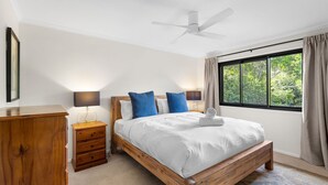 A bedroom with a wooden bed, a ceiling fan, a nightstand with a lamp, a dresser, and a window with curtains. - Gannet's Nest Peregian Beach (Peregian Beach)