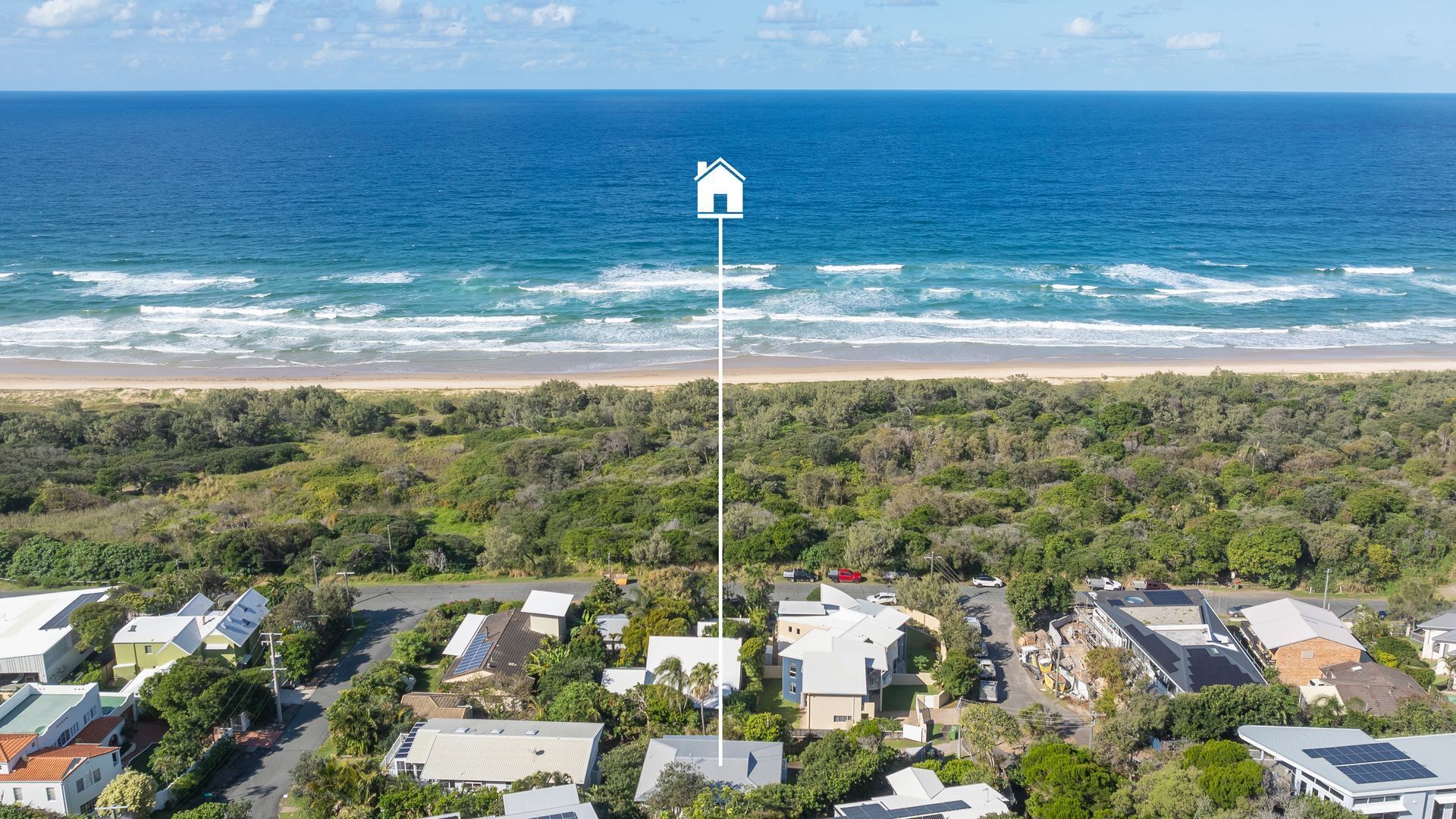 An aerial view of a coastal residential area with houses, a beach, and a clear view of the ocean.