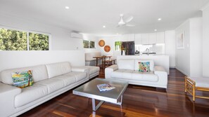 A modern living room with two white sofas, a coffee table, and a dining area with a wooden table and chairs. - Teal Green (Peregian Beach)