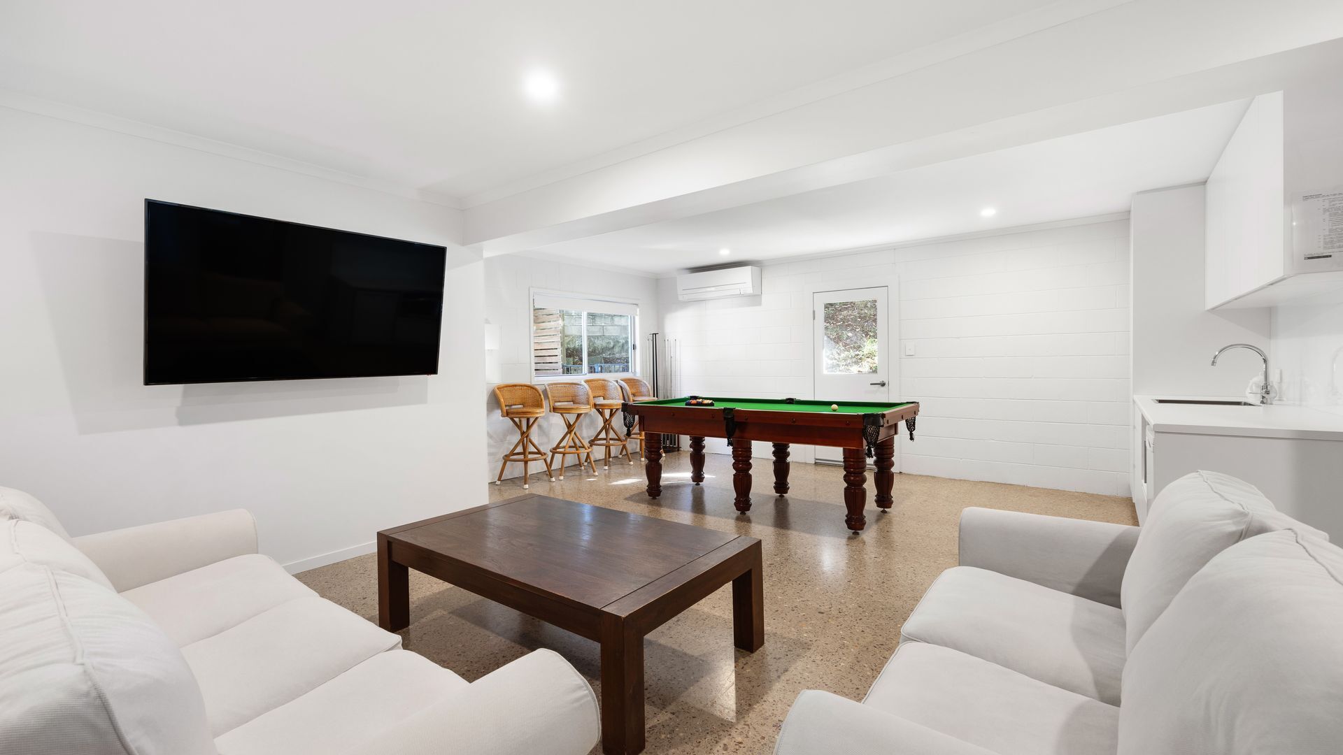 Un salon moderne avec une table de billard, des canapés blancs, un téléviseur à écran plat et un coin cuisine.
