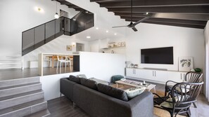 A modern living room with a grey sofa, a coffee table, and a TV. There is a staircase with a black railing leading to an upper level. - Martin's Patch Unit 2 Peregian Beach (Peregian Beach)
