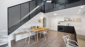 A modern kitchen with a wooden table and white chairs, a black oven, and a white countertop. - Martin's Patch Unit 2 Peregian Beach (Peregian Beach)