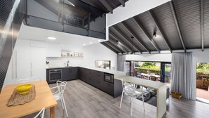 A modern kitchen with a large island, white cabinetry, and a dining area with a wooden table and chairs. - Martin's Patch Unit 2 Peregian Beach (Peregian Beach)