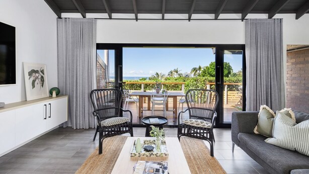 A modern living room with a large sliding glass door leading to an outdoor patio. The room features a sofa, two armchairs, a coffee table, and a dining table with chairs. - Martin's Patch Unit 2 Peregian Beach (Peregian Beach)