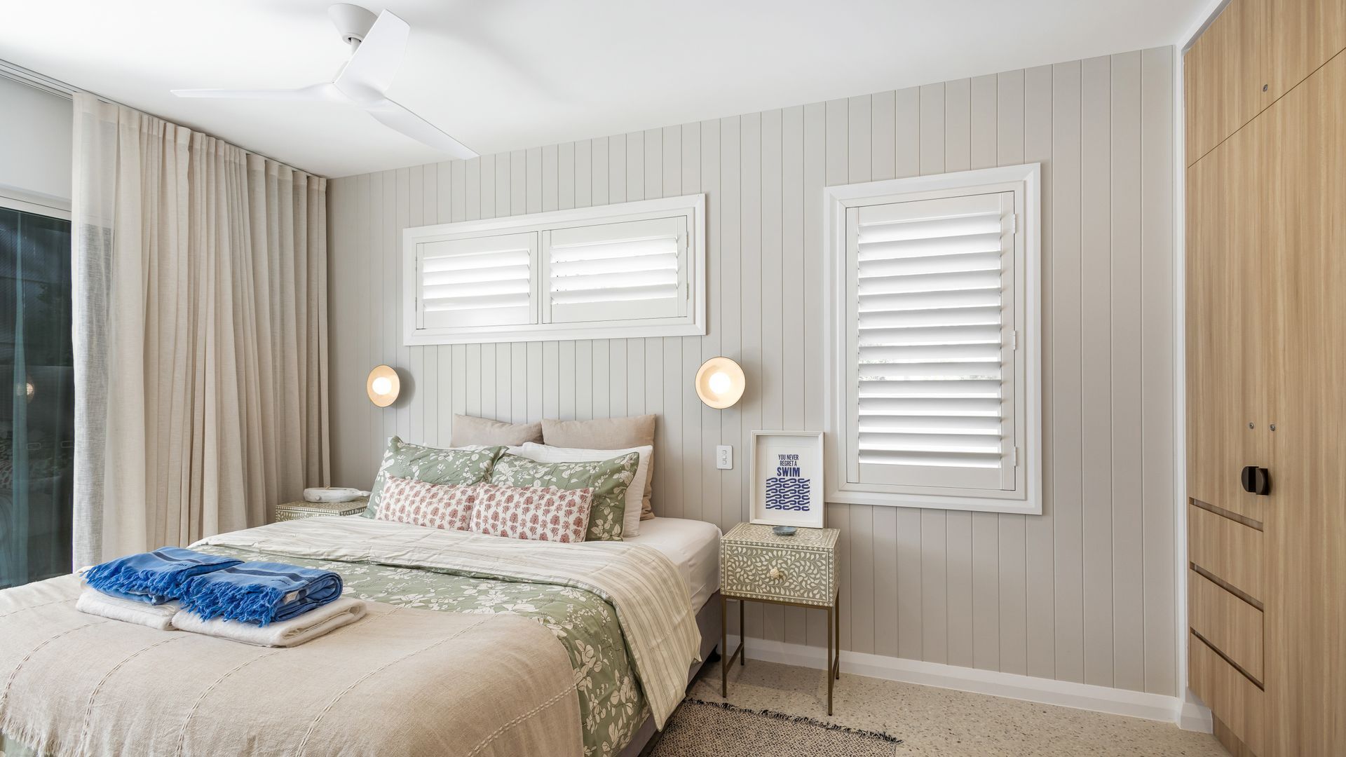 Een slaapkamer met een bed, twee nachtkastjes, een wandlamp en een raam met jaloezieën.