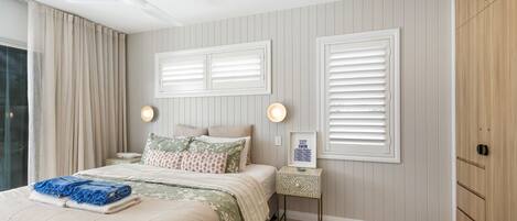 Een slaapkamer met een bed, twee nachtkastjes, een wandlamp en een raam met jaloezieën.