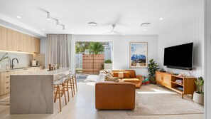 Uma sala de estar moderna com sofá, televisão e uma área de cozinha com balcão.