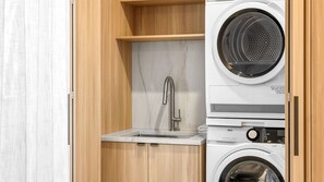 A compact laundry room with a washing machine, a sink, and a wooden cabinet. - Olas by The Sea 2 Peregian Beach (Peregian Beach)