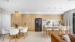 A modern kitchen with a central island, wooden cabinets, and a stainless steel refrigerator. - Olas by The Sea 2 Peregian Beach (Peregian Beach)