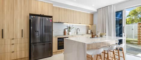 Una cocina moderna con refrigerador de acero inoxidable, gabinetes de madera, encimera de mármol y una barra con taburetes.