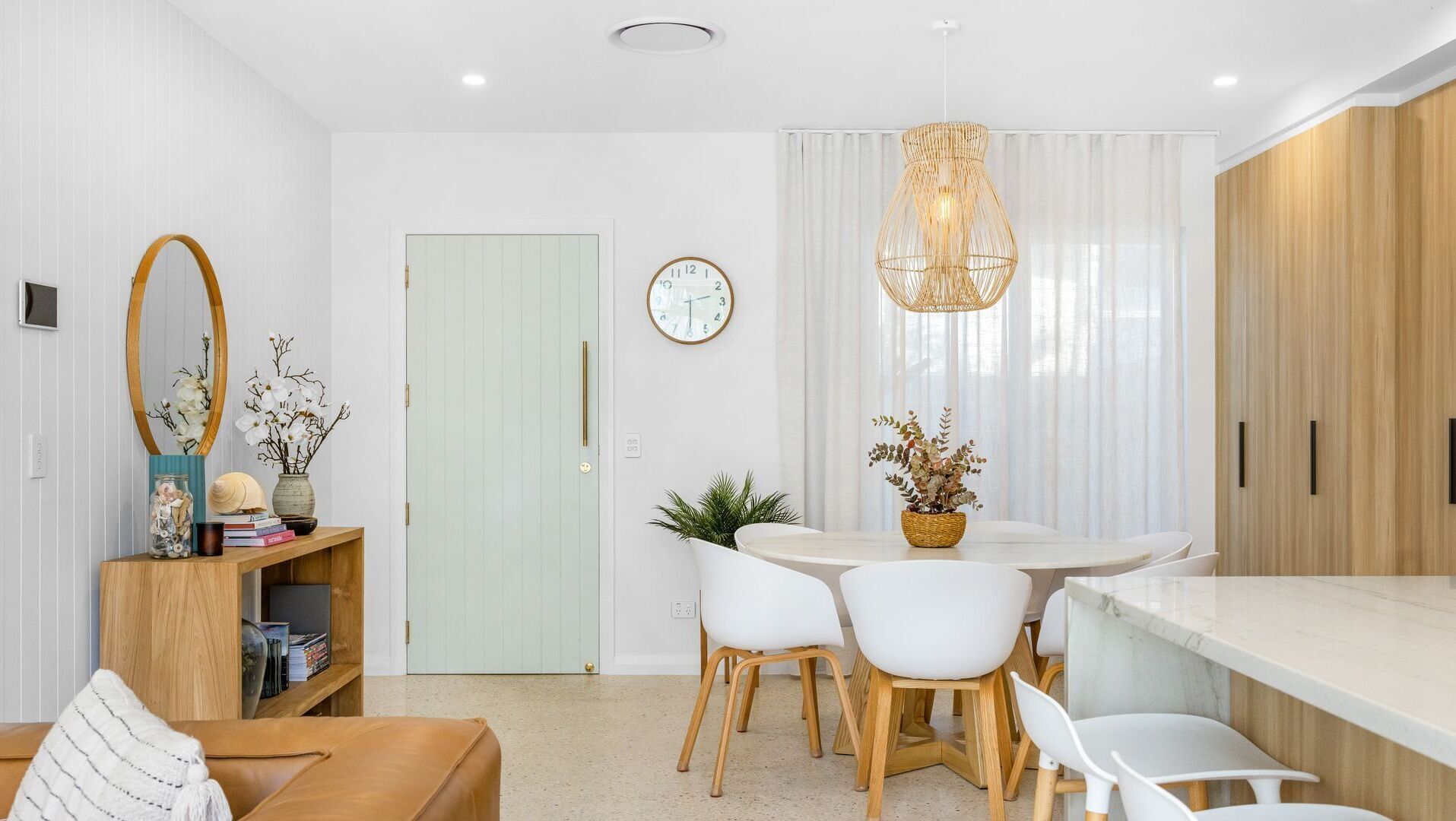 Una cocina moderna con comedor, que incluye una mesa redonda, sillas blancas, un mueble de madera y una lámpara colgante.