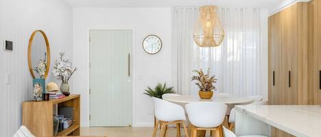 Una cocina moderna con comedor, que incluye una mesa redonda, sillas blancas, un mueble de madera y una lámpara colgante.