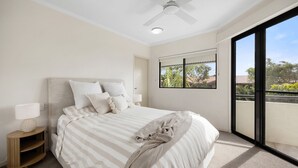 A bedroom with a bed, a nightstand, a ceiling fan, a window with a view, and a balcony. - First Avenue Glade 6 (Coolum Beach)